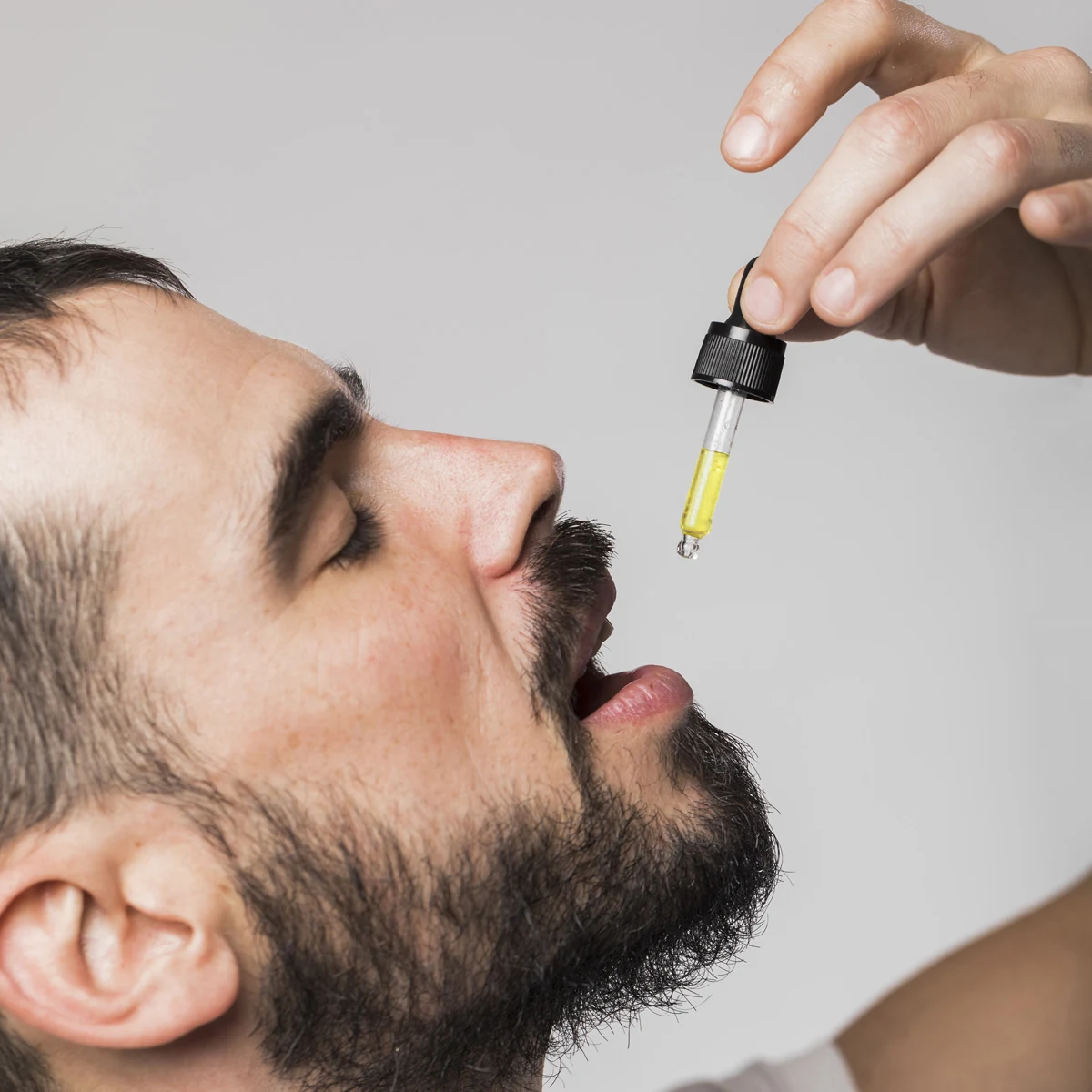 Homme tenant une pipette d’huile au-dessus de sa bouche