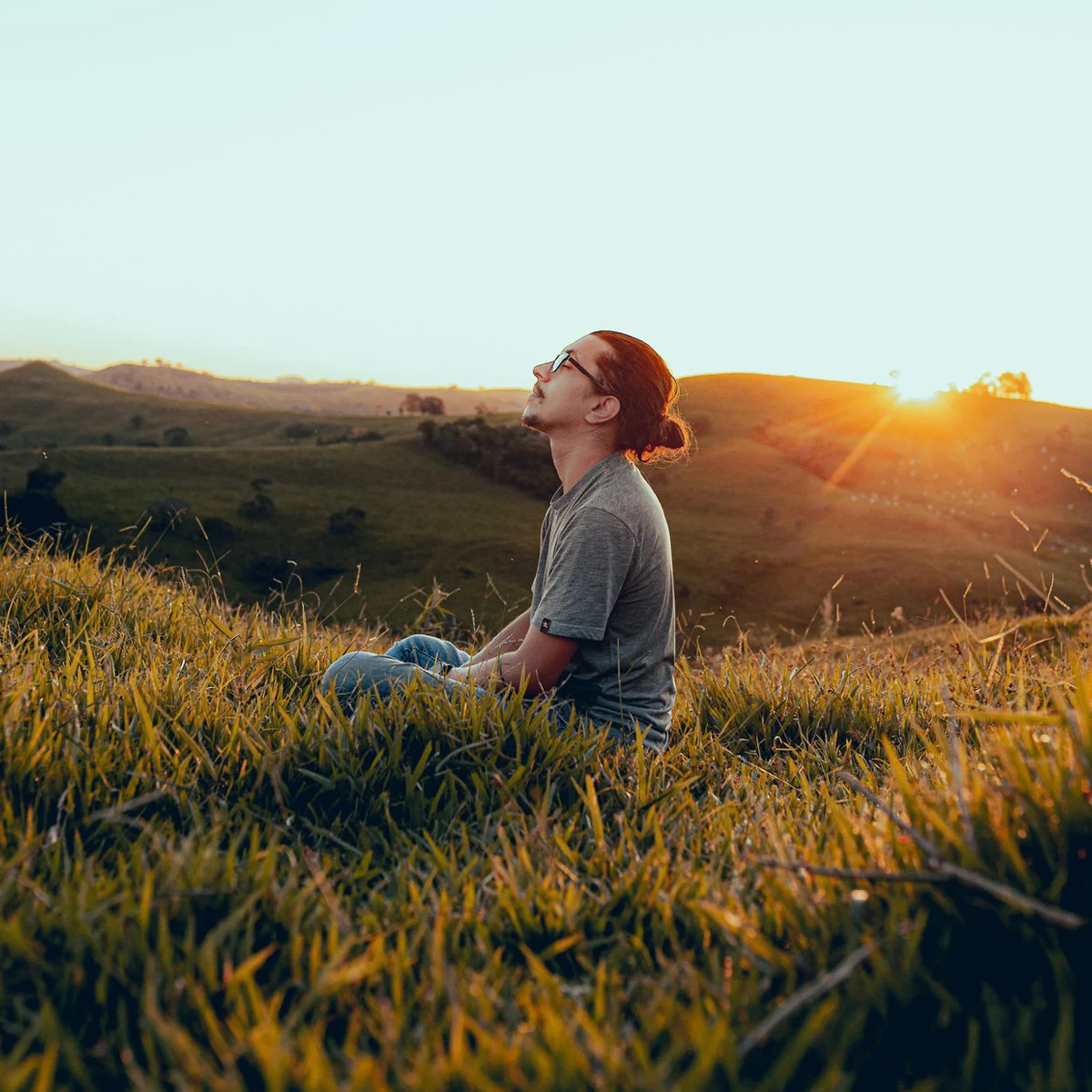 Personne assise dans une prairie au soleil couchant